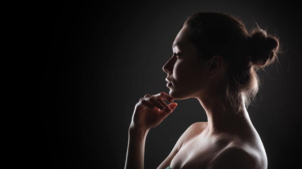 A woman in a dark background with a beautiful neck